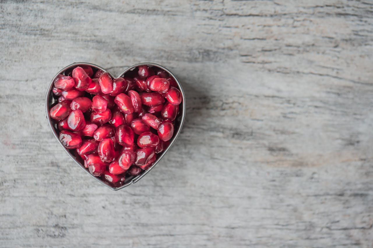 about-04 Delicious and juicy pomegranate seeds in a heart-shaped bowl on a wooden table.